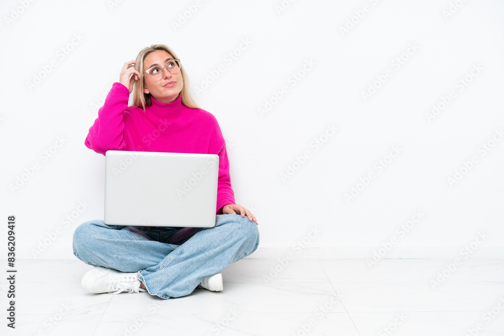 Fototapeta premium Young caucasian woman with laptop sitting on the floor having doubts and with confuse face expression