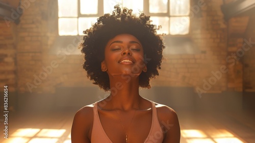 Laughing young woman with afro hair in a tank top, basked in warm sunlight in a room with brick walls