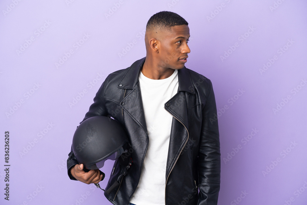 Latin man with a motorcycle helmet isolated on purple background looking to the side Latin man with a motorcycle helmet isolated on purple background looking to the side