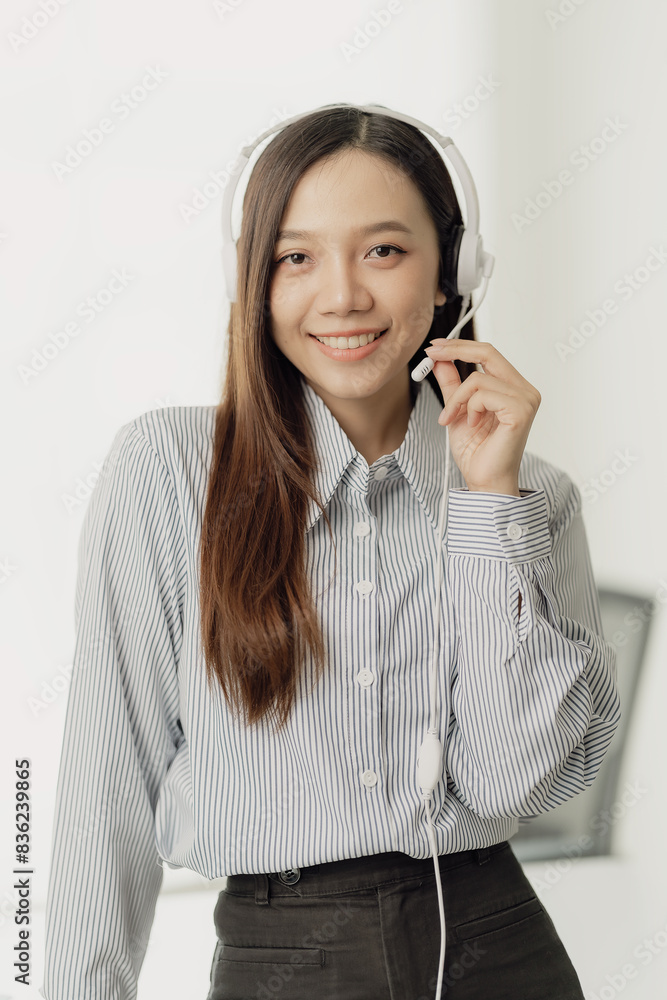 Beautiful Asian female salesperson or call center operator wearing a wireless headset is talking with a customer on the phone. Provide advice and communicate with customers via computer video calls.