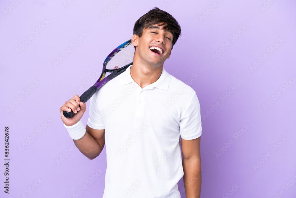 Handsome young tennis player man isolated on ocher background laughing Handsome young tennis player man isolated on ocher background laughing