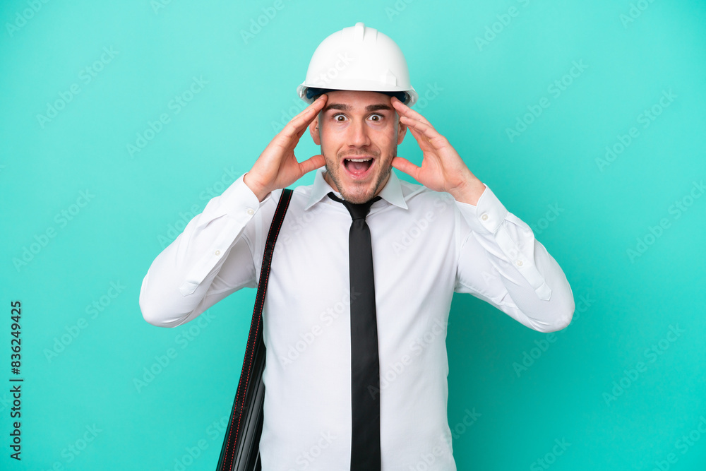 Young architect caucasian man with helmet and holding blueprints isolated on blue background with surprise expression Young architect caucasian man with helmet and holding blueprints isolated on blue background with surprise expression