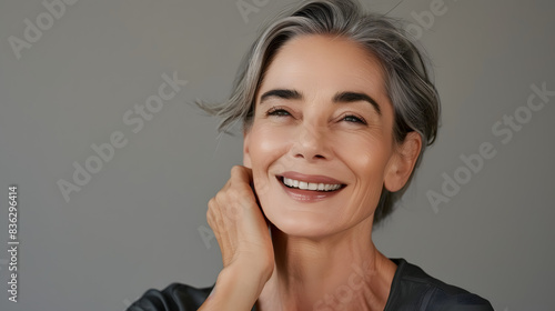 Beautiful face and smiling mature woman with shining anti-aging cosmetics and dermatology on grey studio background. Beautiful woman with confidence, happiness, and self-care