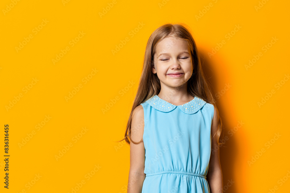 Little girl with closed eyes and a joyful smile standing against a vibrant orange wall on a sunny day Little girl with closed eyes and a joyful smile standing against a vibrant orange wall on a sunny day