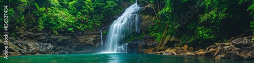 Amidst an idyllic scene, a flowing waterfall splashes through lush jungle, epitomizing tropical beauty.