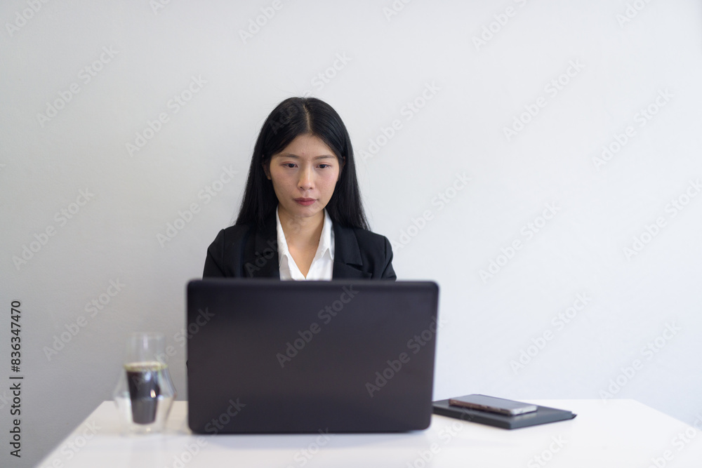 Asian businesswoman with laptop working in office, coffee and notebooks on desk. Professional setting. Asian businesswoman with laptop working in office, coffee and notebooks on desk. Professional setting.