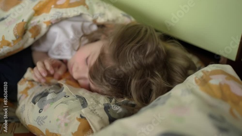 Child lies under blanket in bed and tries to fall asleep. Concept Rest, coziness, childishness