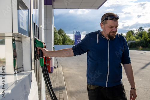 A man standing next to a gas pump filling up his vehicle with fuel at a gas station.