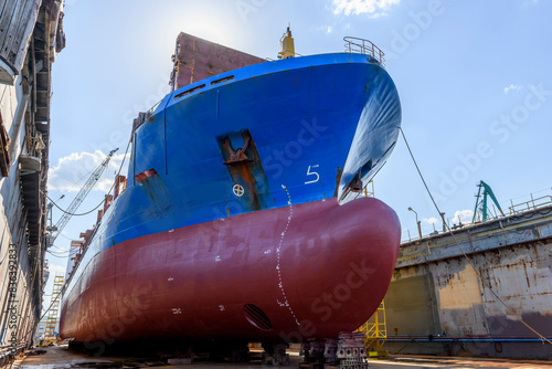 Cargo vessel in dry dock on ship repairing yard. Bulbous bow.