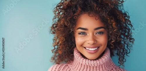 Woman With Curly Hair Smiling in Pink Sweater Against Blue Background