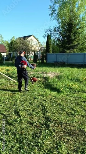 a man mows the grass in the garden. vertical video