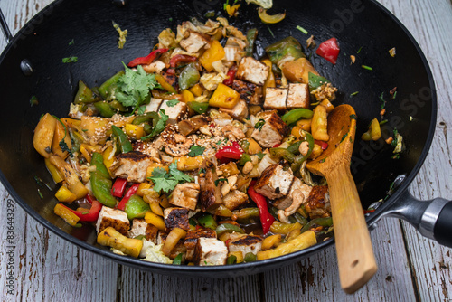 Vegan pepper, tofu and zucchini stir fry in wok, wooden table,