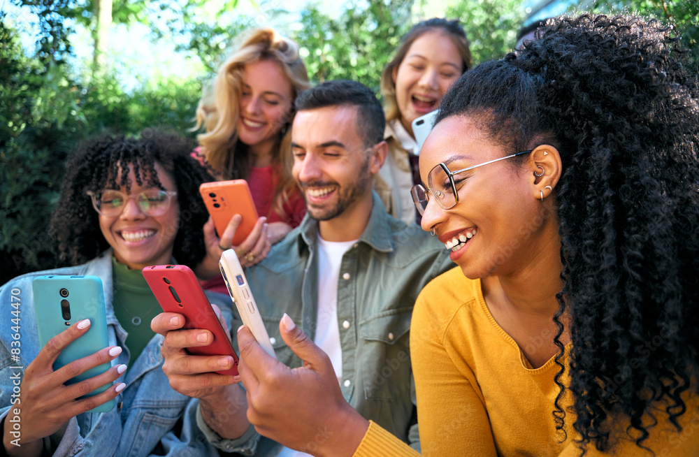 Group of smiling young friends using smart mobile phones app together. Millennials addicted to technology trends. University students and Social media online community. Focus on the Latina woman Group of smiling young friends using smart mobile phones app together. Millennials addicted to technology trends. University students and Social media online community. Focus on the Latina woman