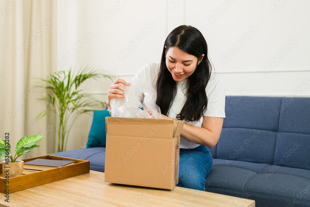 Beautiful woman unpacking a recently delivered package in her cozy living room and looking happy Beautiful woman unpacking a recently delivered package in her cozy living room and looking happy