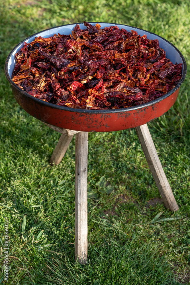 A full red casserole of red dried chili peppers that show off the texture and concept of the spice ingredients. The pan is placed on a wooden stool that has three legs. A full red casserole of red dried chili peppers that show off the texture and concept of the spice ingredients. The pan is placed on a wooden stool that has three legs.