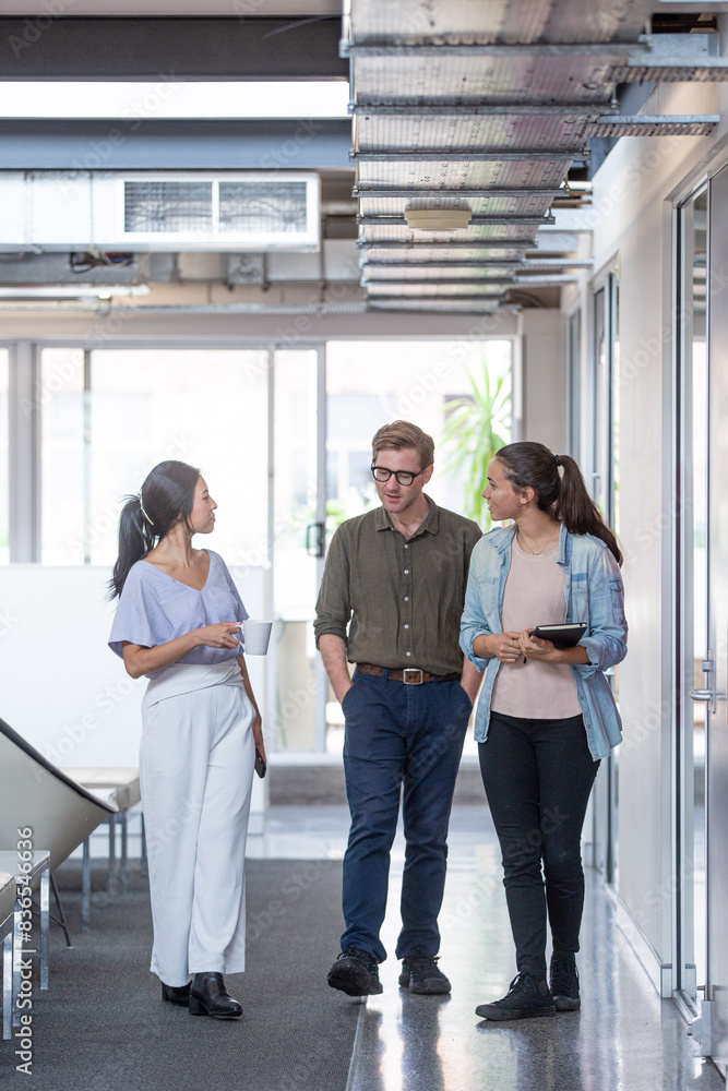 Three businesspeople walking through office hall and talking Three businesspeople walking through office hall and talking