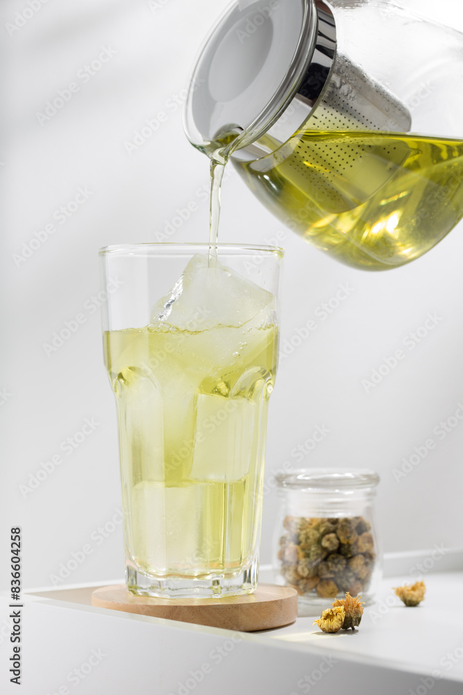 A hand pours a refreshing chrysanthemum tea over ice in a clear glass. A hand pours a refreshing chrysanthemum tea over ice in a clear glass.