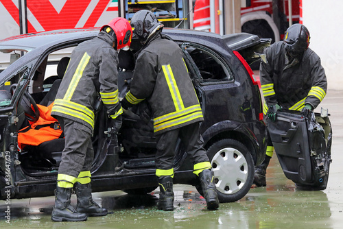 firefighters unhinging the stuck door of a crashed car after the collision to free the injured person from the sheet metal counters
