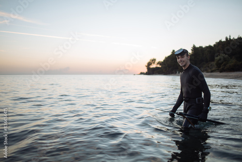 Young active man in wetsuit holds spear gun in water photo