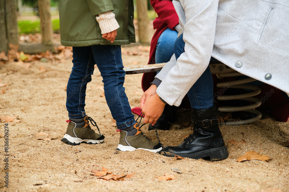 Unrecognizable mother lacing up her son shoelaces at the children's playground. Unrecognizable mother lacing up her son shoelaces at the children's playground.
