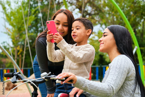 Boy showing something to his mothers on the phone in a park. LGBT family.