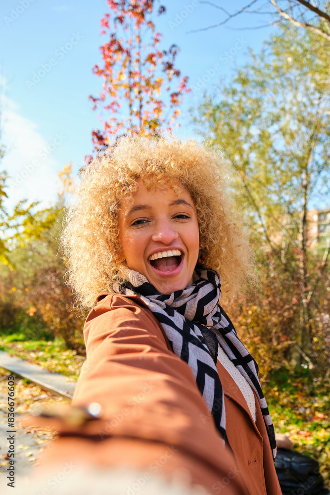 Happy young Brazilian woman smiling and taking a selfie in a park in autumn. Happy young Brazilian woman smiling and taking a selfie in a park in autumn.