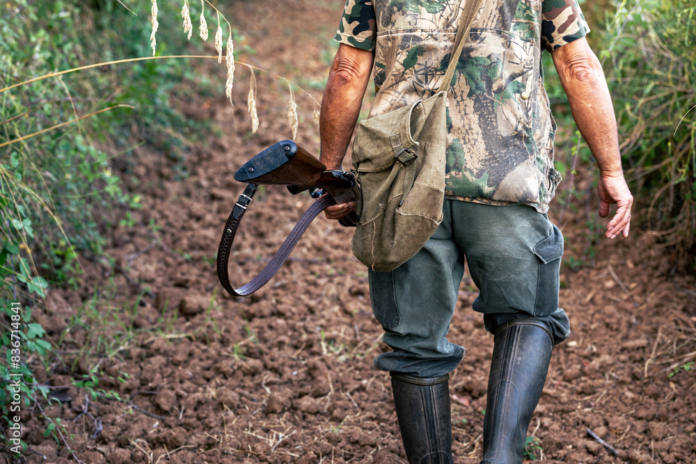 Rear view of a mature male with a camouflage outfit and a gun in a forest Rear view of a mature male with a camouflage outfit and a gun in a forest