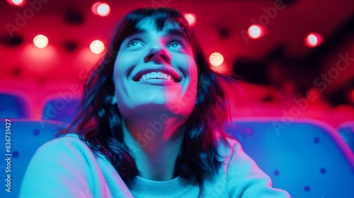 A woman with a smile gazes upward with colorful lighting in a theater. The red and blue lights create a vibrant atmosphere around her. © Natalia
