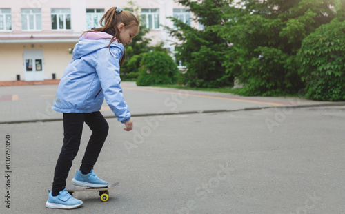 Pretty little girl learning to skateboard on beautiful summer day in a school yard. Child enjoying skateboarding ride outdoors.