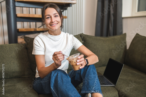 Contented young woman sitting on the sofa and eating dessert