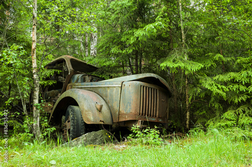 Abandoned car in the forest, Rusty cabin of an old truck is visible from behind the trees in lush green forest, Båstnäs Car Cemetery in Värmland, Sweden