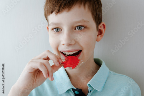Smiling little child boy holds metal bright and colorful plate for align the teeth and bite. Orthodontist treats teeth