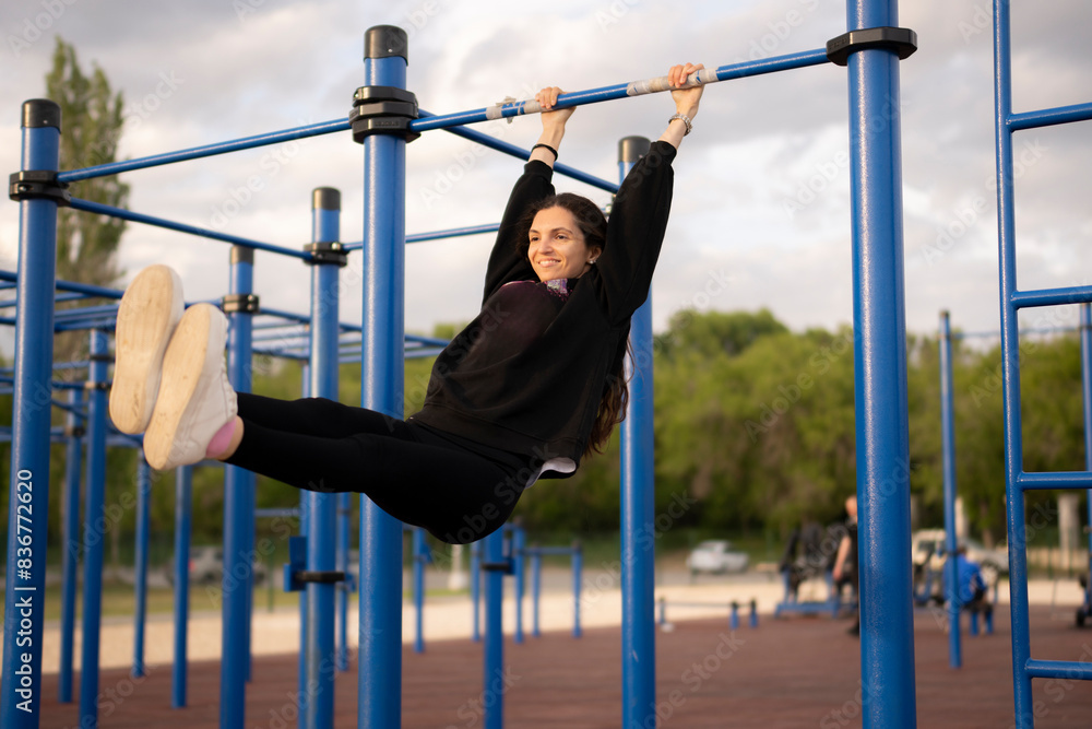 Fototapeta premium Young Female Athlete Hanging on the Bar on Outdoor Exercise Equipment