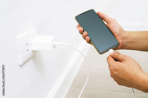 close up hand plugging adapter charge the battery with outlet socket plug and hold mobile phone on wall ,electric safety concept © methaphum