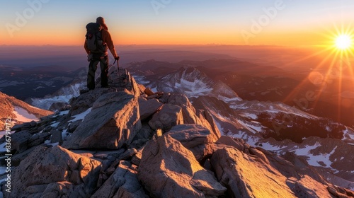 A lone hiker stands on the summit of a mountain, overlooking a breathtaking sunrise over a snow-capped landscape © Ilia Nesolenyi