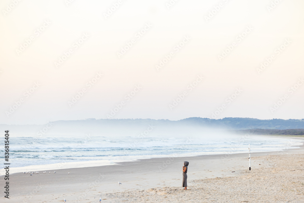 Solo person in hooded robe meditating on the beach at sunrise Solo person in hooded robe meditating on the beach at sunrise