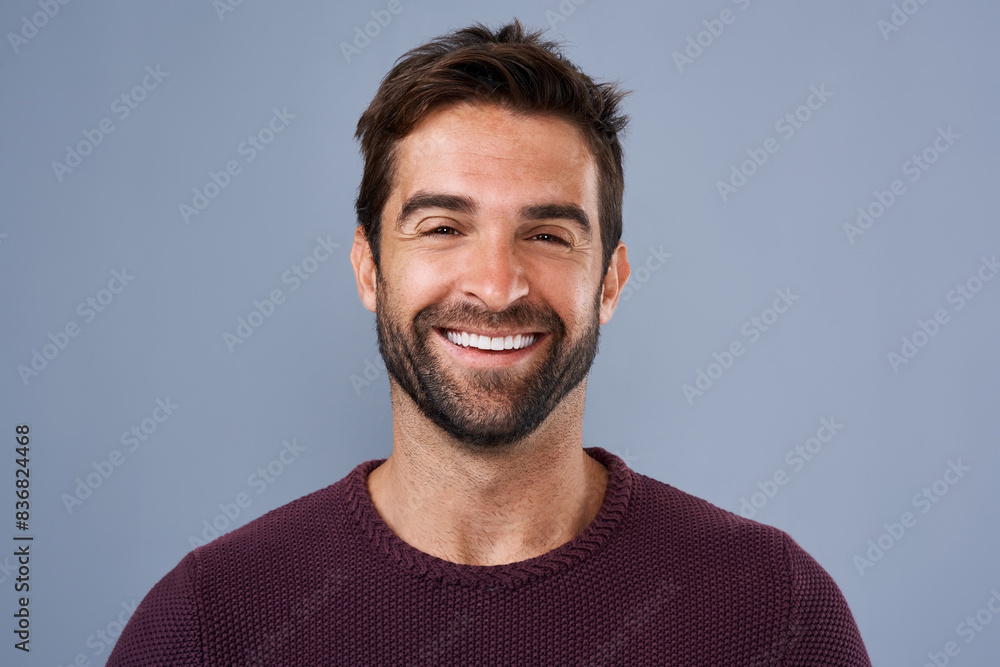 Fototapeta premium Fashion, face and joy of man in studio, sweater and warm for winter in Canada, happy and discount. Blue background, portrait and smile of person, sale and cardigan of cotton, clothes and jersey
