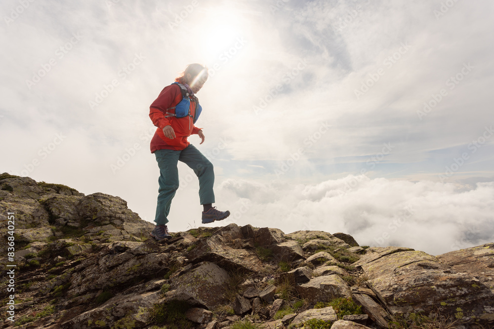 A woman in a red jacket is walking up a rocky mountain