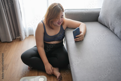 Obese asian woman dieting Weight loss in sportswear using smart phone after workout for weight control at home wellness health.