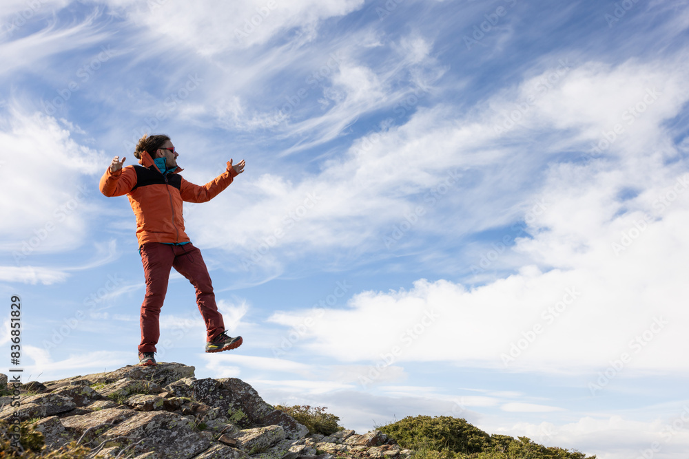 A man in an orange jacket is standing on a rock and looking up at the sky A man in an orange jacket is standing on a rock and looking up at the sky