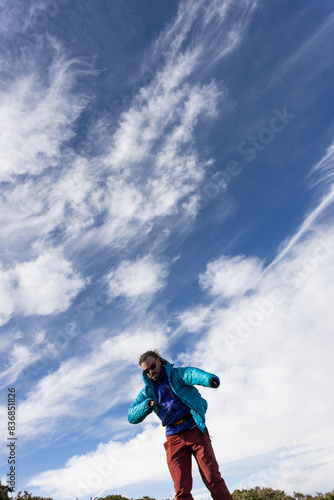 A woman in a blue jacket stands in front of a blue sky with clouds