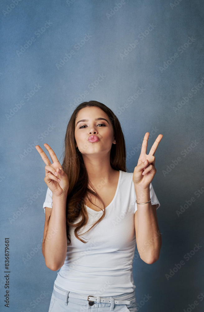 Peace sign, kiss and portrait of woman in studio for romance, affection and gratitude. Beauty, confidence and face of person with flirting emoji, positive hand gesture and love on blue background Peace sign, kiss and portrait of woman in studio for romance, affection and gratitude. Beauty, confidence and face of person with flirting emoji, positive hand gesture and love on blue background