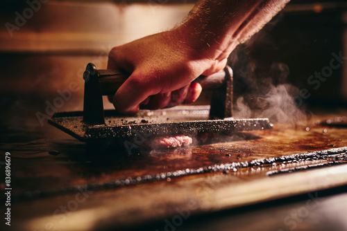 Beef patties being pressed with an iron on a hot grill plate 