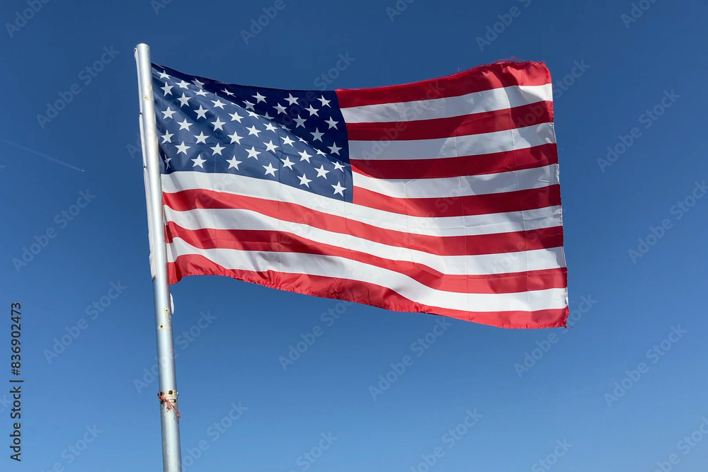 Obraz premium United State of America flag flutters in the wind on blue sky background, Travel and tourism in USA concept, election in USA 2024