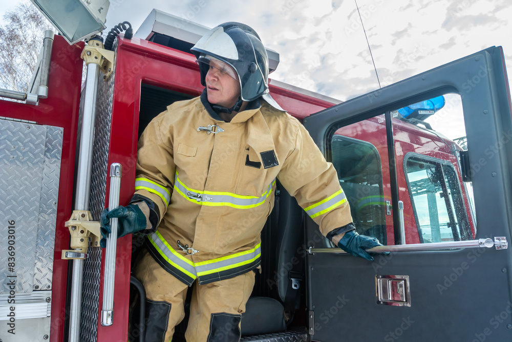 A firefighter in a helmet and protective clothing opened the door of a fire truck. A firefighter gets out of a fire truck to start extinguishing the fire. The rescue service. A firefighter in a helmet and protective clothing opened the door of a fire truck. A firefighter gets out of a fire truck to start extinguishing the fire. The rescue service.