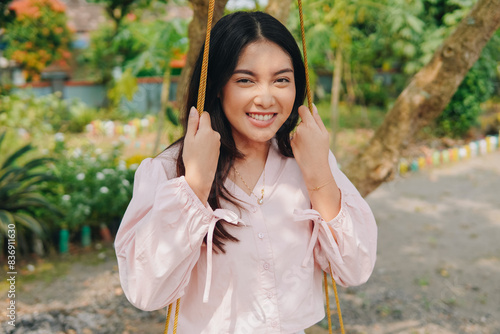 Beautiful young Asian wearing casual outfit smiling to the camera sitting and playing on a swing during weekend break.