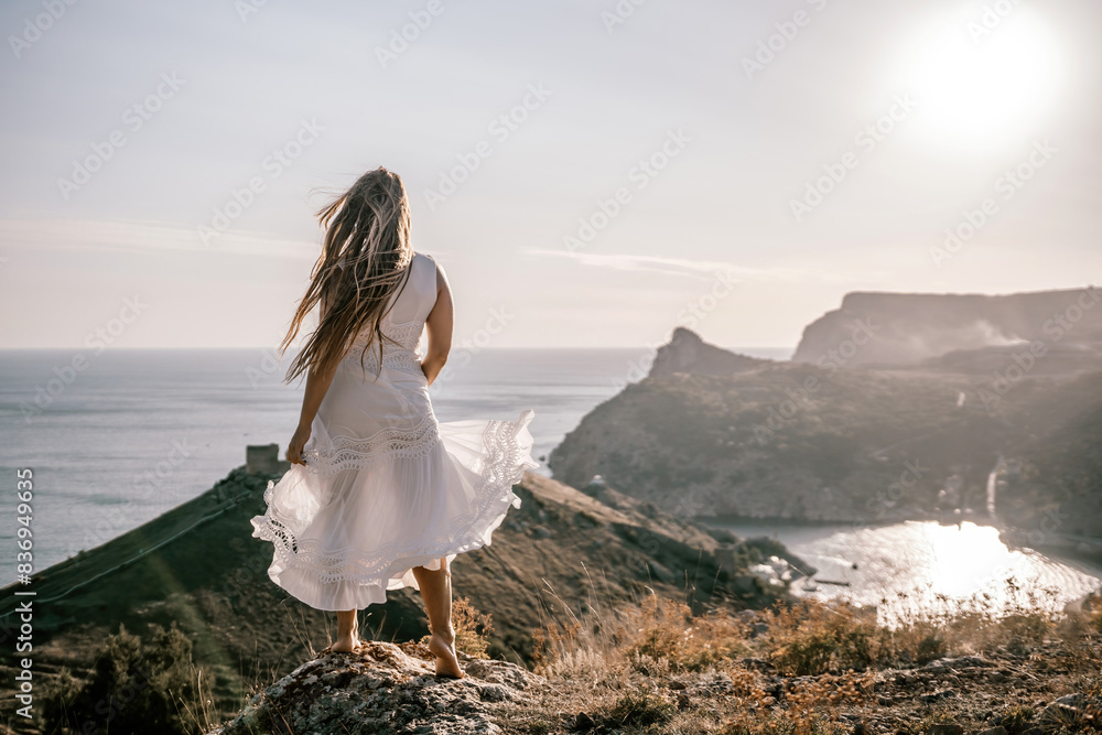 A woman in a white dress stands on a hill overlooking the ocean. The scene is serene and peaceful, with the woman's dress billowing in the wind. The combination of the ocean.