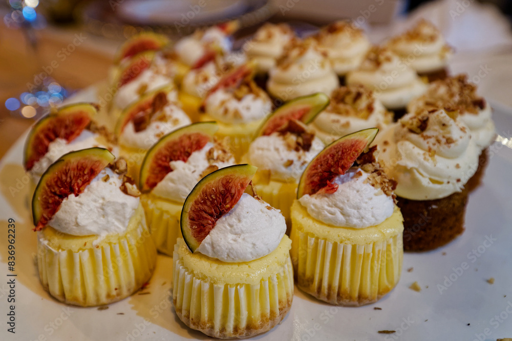 A plate full of small cupcakes with cream and fig pieces toppings. A plate full of small cupcakes with cream and fig pieces toppings.