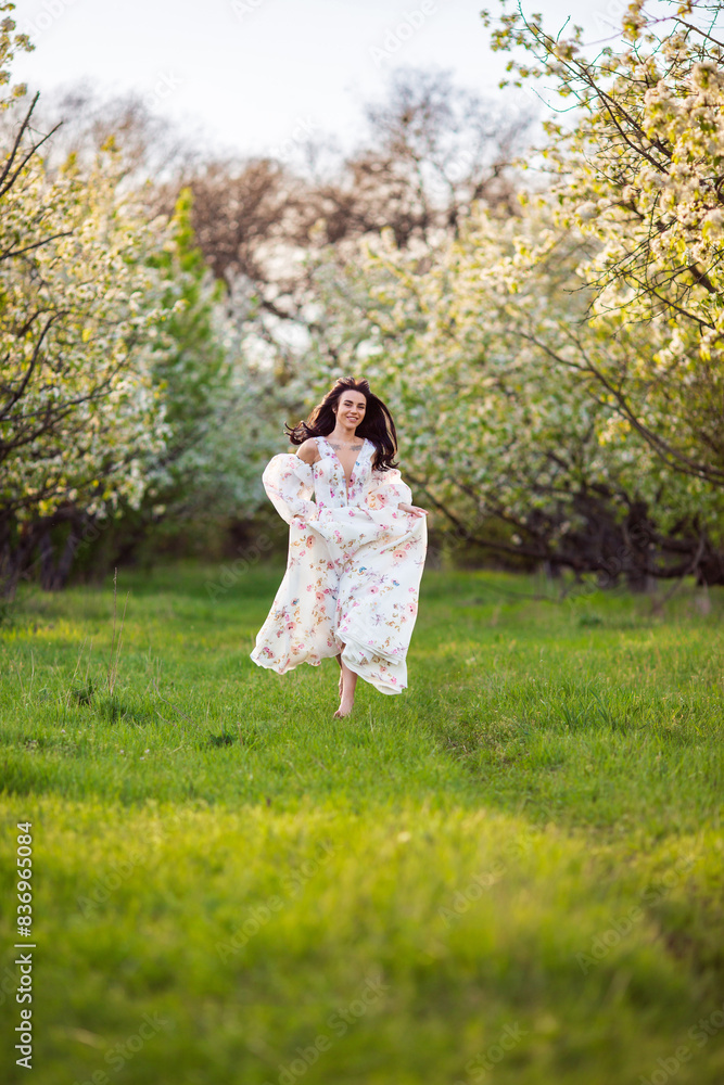 Full-length portrait of a beautiful brunette caucasian woman running in blossoming apple garden in white floral dress on a fresh green grass shot from her face with her hair flying Full-length portrait of a beautiful brunette caucasian woman running in blossoming apple garden in white floral dress on a fresh green grass shot from her face with her hair flying