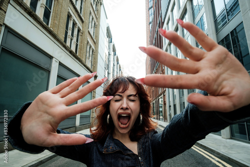 Young woman screaming in the street with eyes closed and hands up.